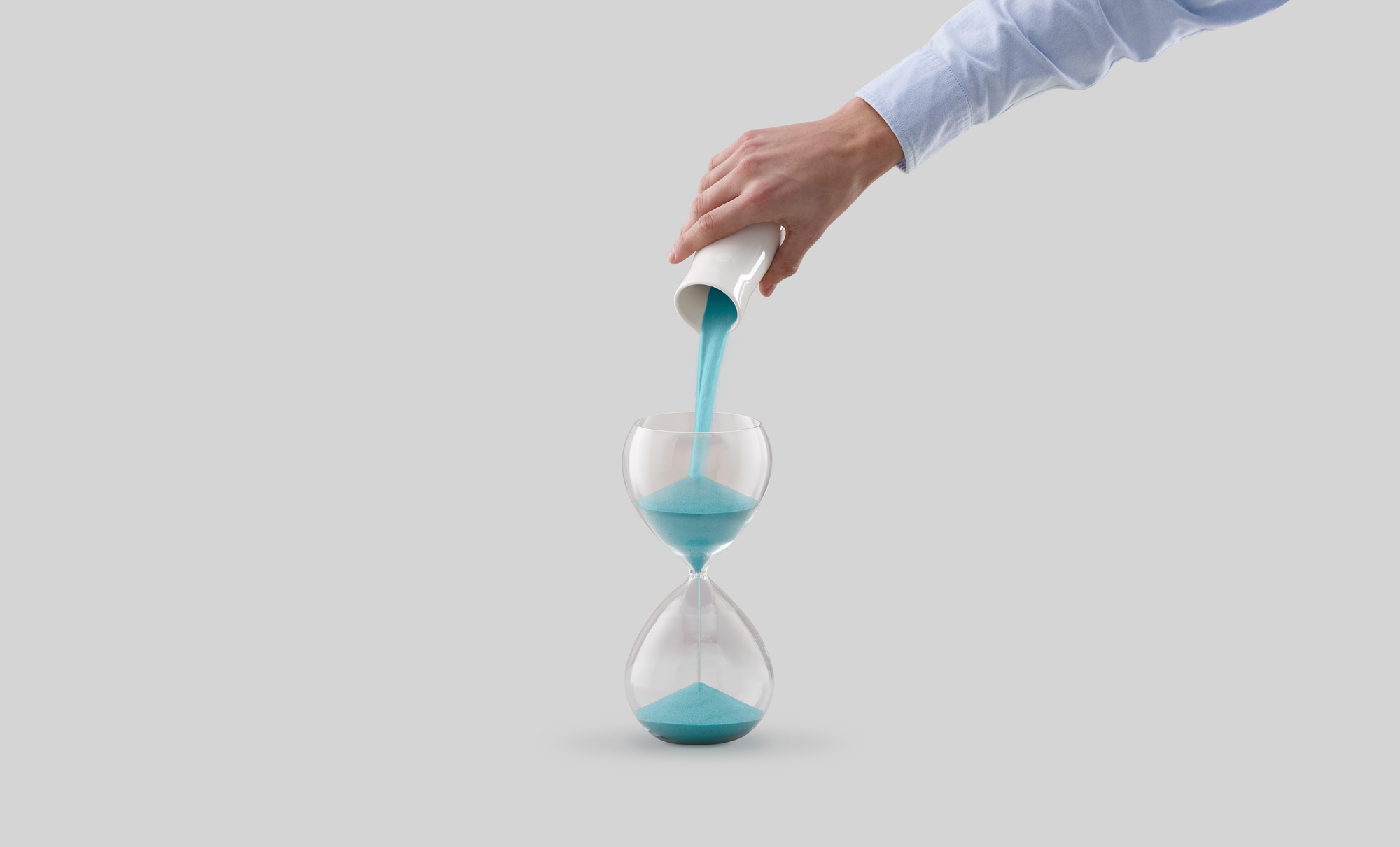 A hand pouring more sand into the top of an hourglass